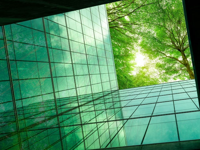 Modern glass office building with green tinted windows and curved architecture against a blue sky