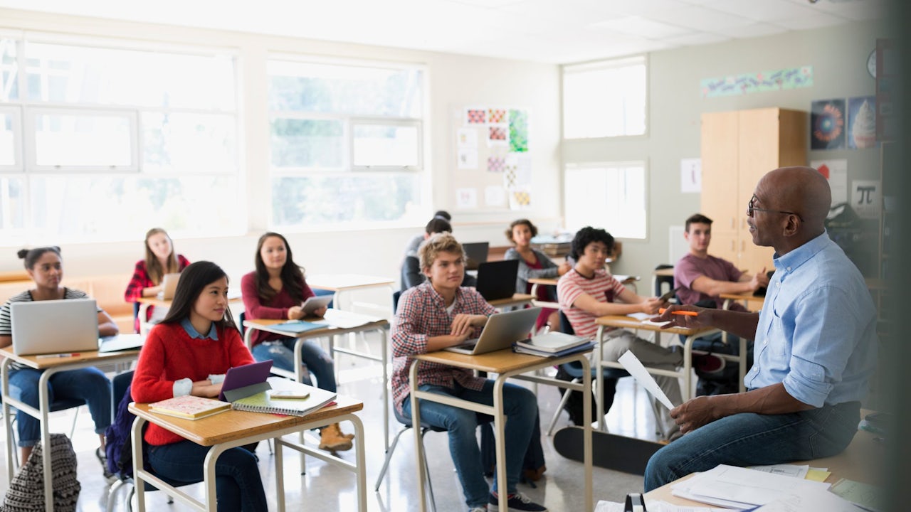 High school students listening to a teacher in a classroom.