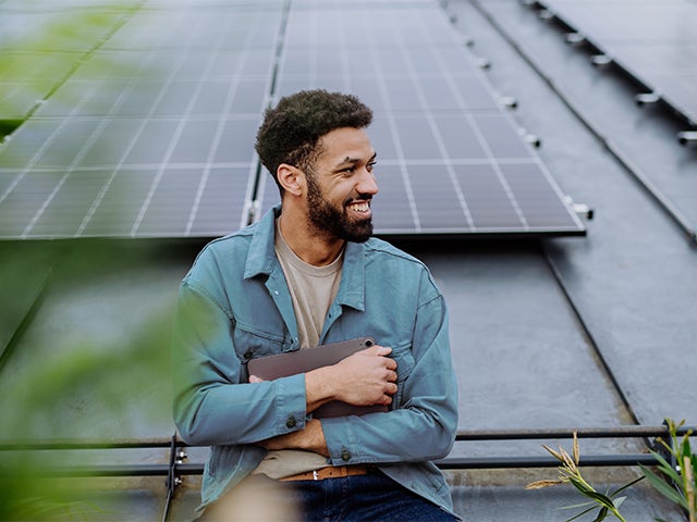 A student stands in front of solar panels, possibly on a college campus.