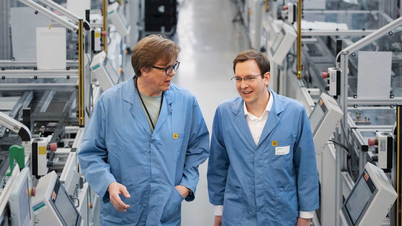 Two employees walk and talk on the shop floor at Siemens Electronics Factory, Erlangen.