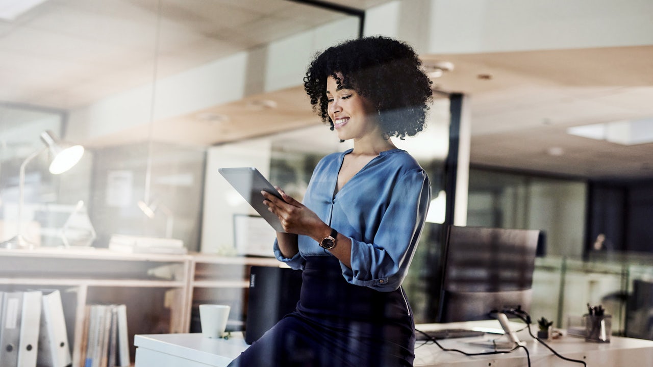 A woman with curly hair stands and looks at a tablet. 