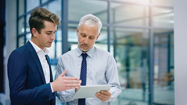Two men having a conversation about information shown on a tablet device.