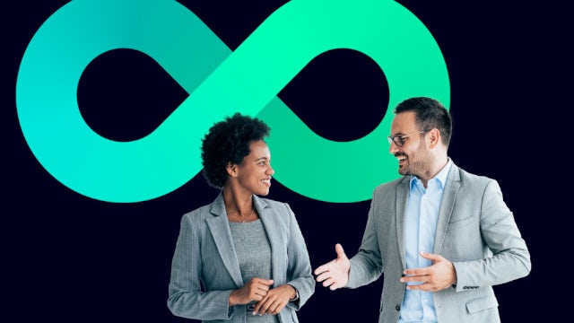 Two professionals in business attire having a conversation in front of the Siemens large green infinity symbol on a dark blue background.