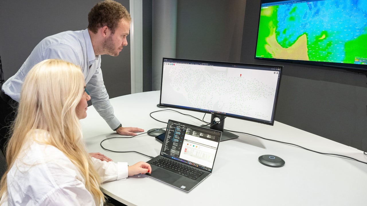 Two grid operators view system status on a computer.