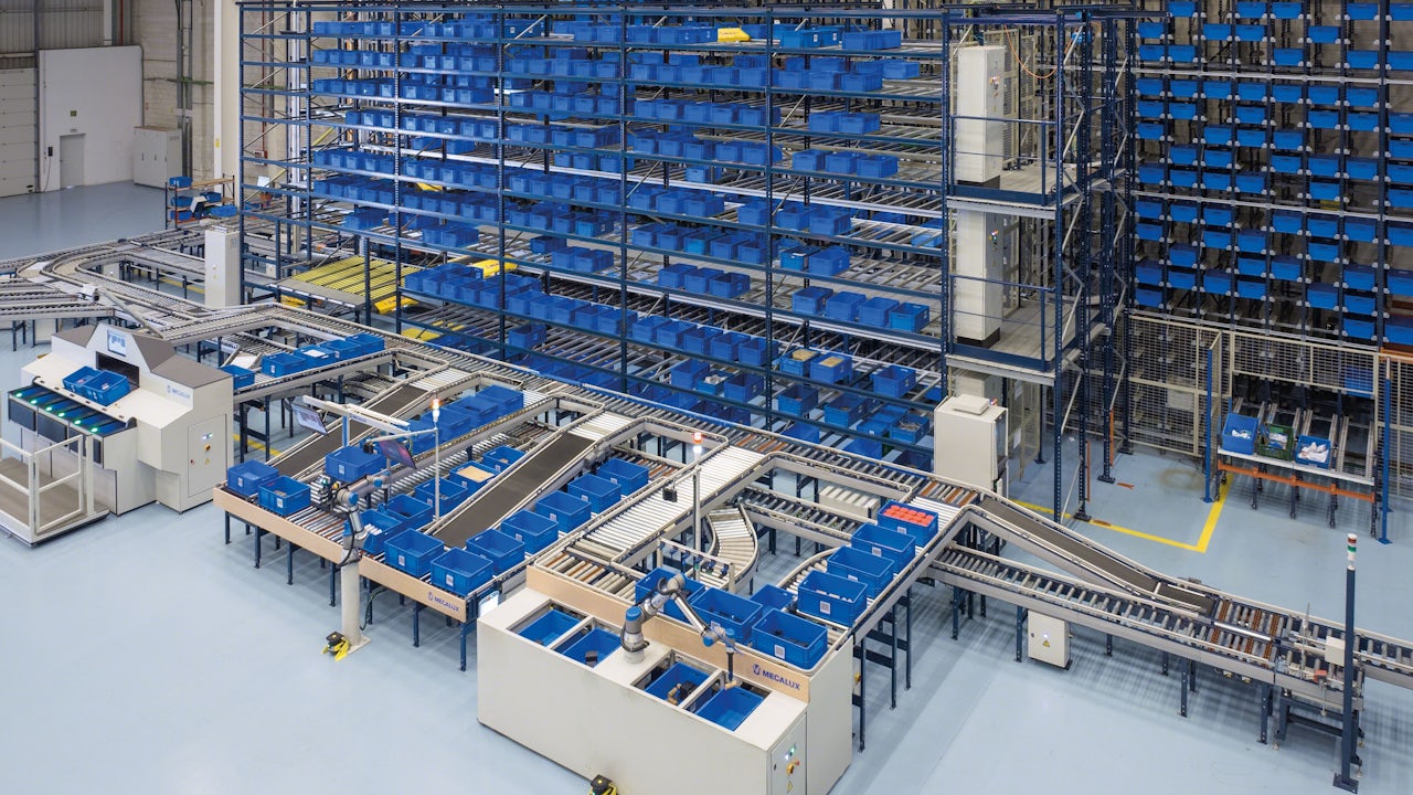 A warehouse with a robot picking up a box from a pallet. 
