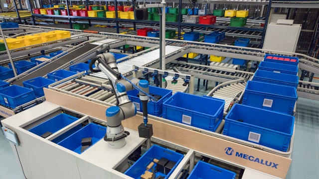 A robotic arm sorts items into blue bins on a conveyor belt system in a busy warehouse filled with colorful storage containers.
