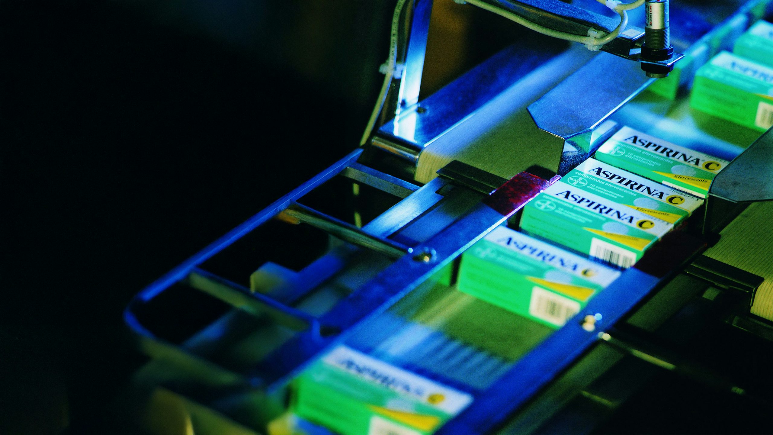 The image shows an automated manufacturing line for packaging aspirin tablets.