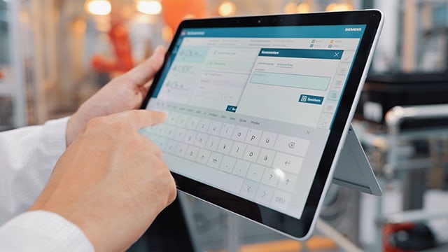 Close up of a person holding a tablet and pointing at it.