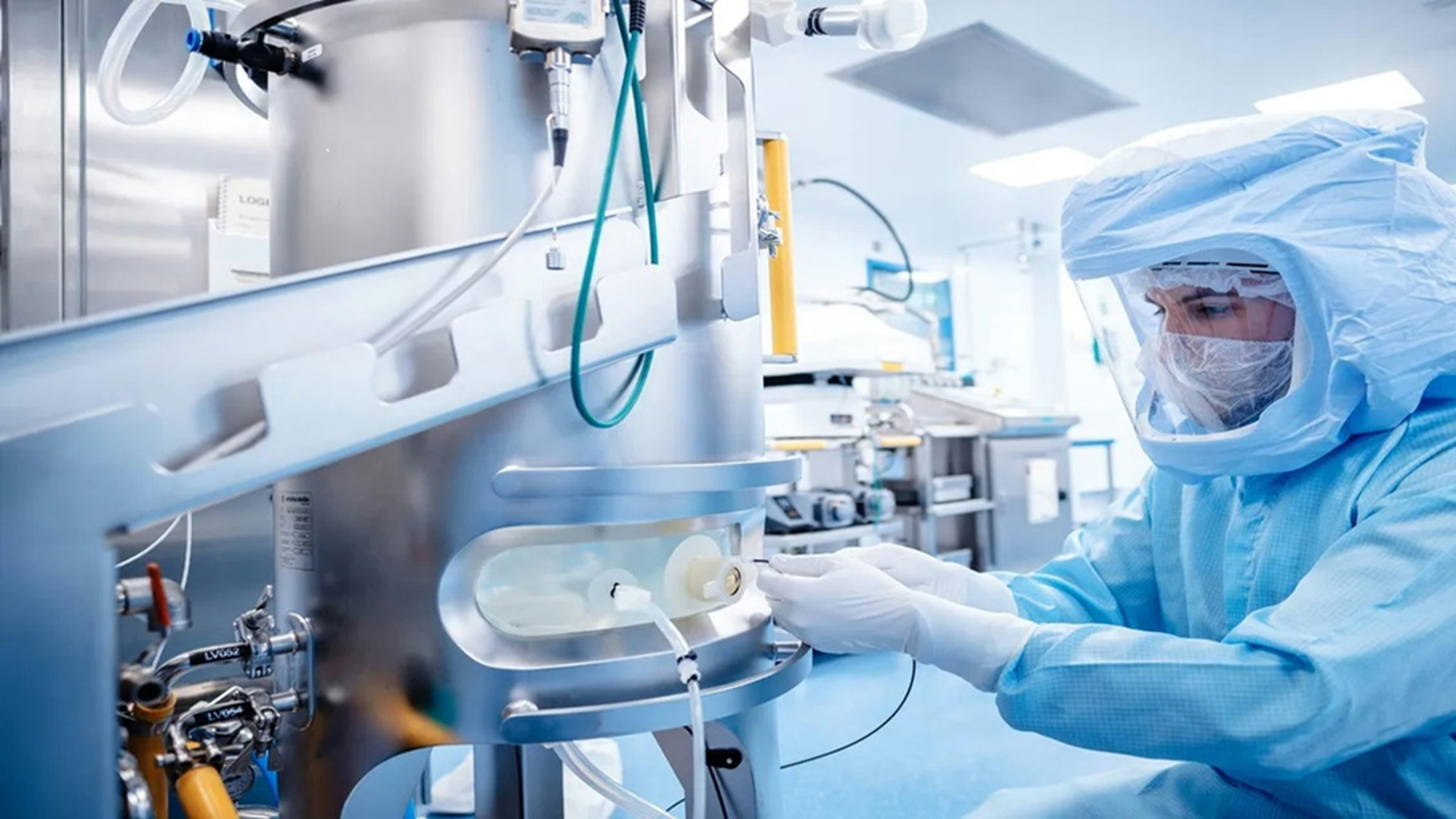 Person in a full cleanroom suit working with a large piece of stainless steel industrial equipment.