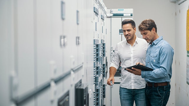 2 people standing in front of data servers working on a tablet device.