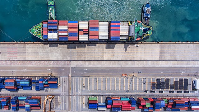 A container ship is docked at a port with a large crane in the background.
