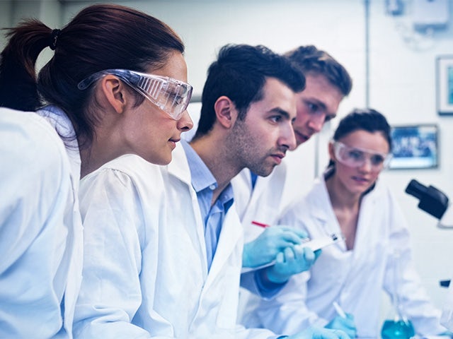 A group of engineers wearing lab coats looking at a computer screen.