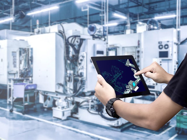 A man holding a tablet with a plant simulation on the screen while standing in a medical device manufacturing facility.