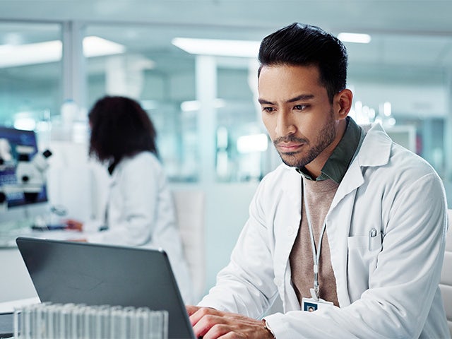 Man wearing a lab coat in a pharmaceutical lab looking at a computer.