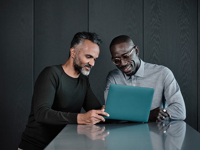 Two colleagues collaborating and smiling as they review content on a laptop in a contemporary office setting.