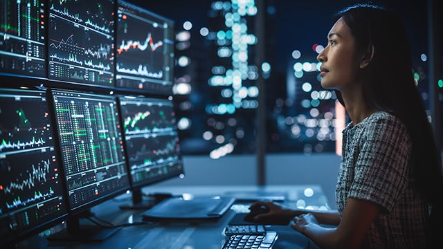 A woman sits in a dark room full of computer monitors