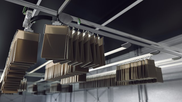 An automated overhead conveyor system transports numerous brown packages hanging from individual carriers through a dark, industrial space.