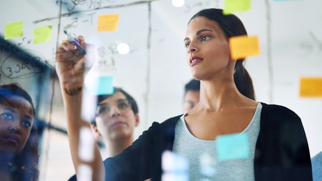 Woman writes on glass and uses sticky notes during meeting.