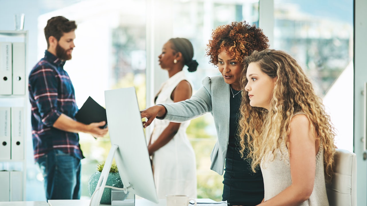 A colleague points something out on a computer with two other coworkers in the background. 