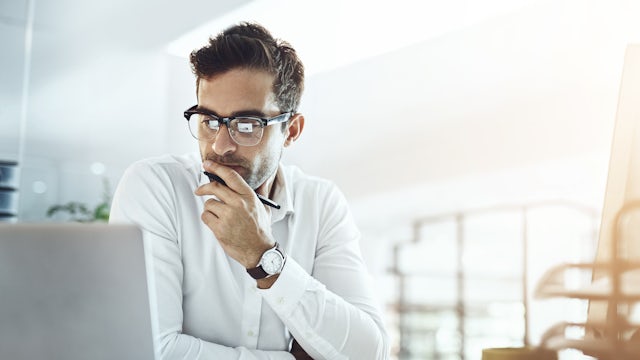 Man wearing glasses sits in front of a laptop.