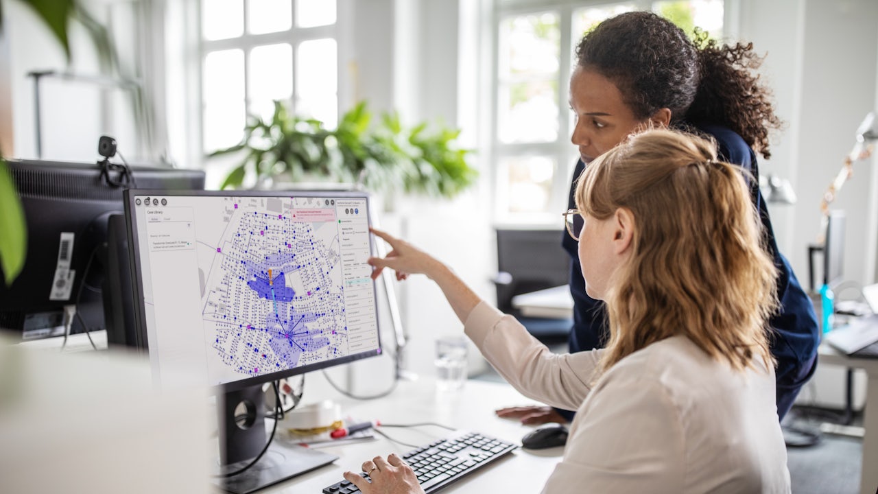 Two business women look at a Gridscale X LV Management map on a computer. 