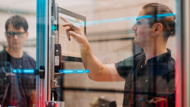 A Siemens industrial copilot is shown in a factory setting with a digital interface and a robotic arm.