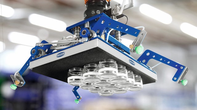 A robotic arm with an orange joint and blue frame holds a large, flat gray suction gripper that is lifting multiple small, clear glass jars. The background is a brightly lit industrial setting.