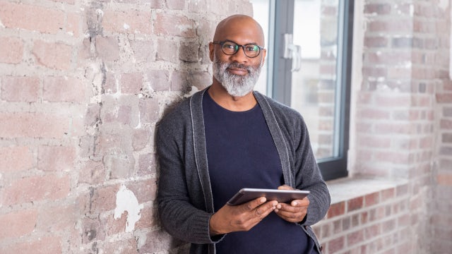 Person using a tablet while leaning against a brick wall, accessing digital learning and online training content.