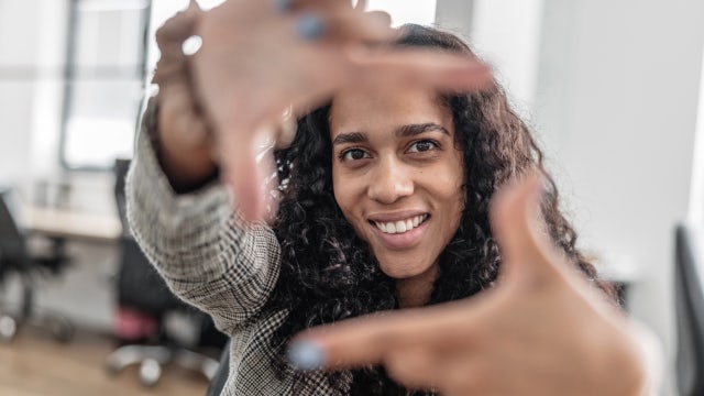 Smiling professional woman holding her fingers in front of her face in a square to form a window.