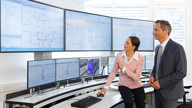 A control room with a person operating a computer and a large monitor displaying a graph.