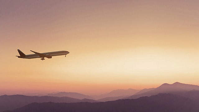 Plane flying in front of a sunset and clouds.
