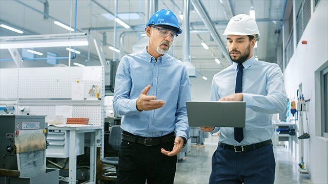 Two men talking and looking at a tablet. 