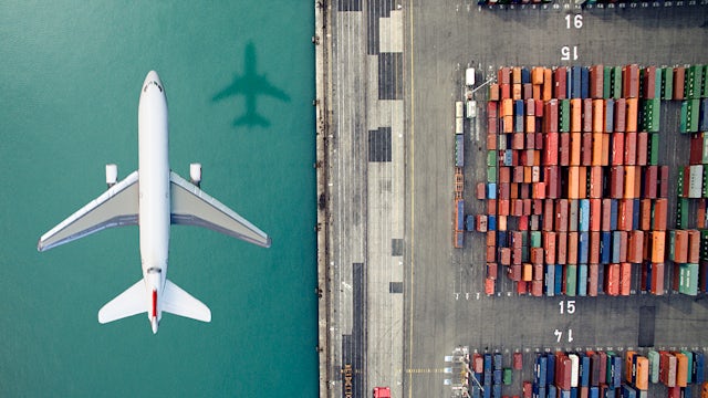 The image shows a plane flying over cargo containers in the water.