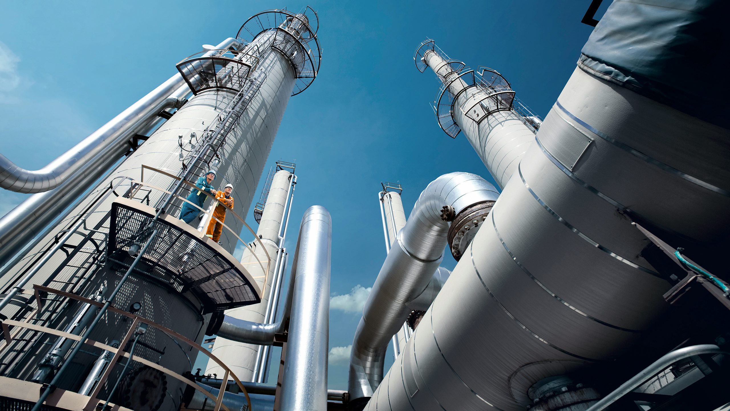 A large industrial facility with multiple tanks and pipelines, possibly a tank farm or terminal, under a clear blue sky.