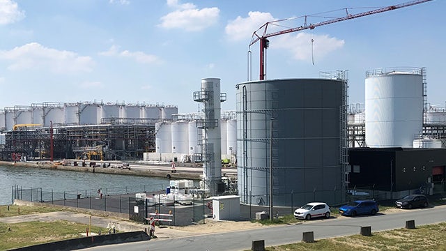 A photo of a large industrial facility with multiple tanks and pipelines in an urban setting.