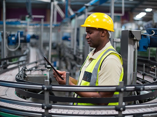 Person wearing safety glasses and hard hat examining a machine part in an industrial setting