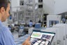 A male overseeing a factory production environment and analyzing the throughput on an iPad using Plant Simulation X software.
