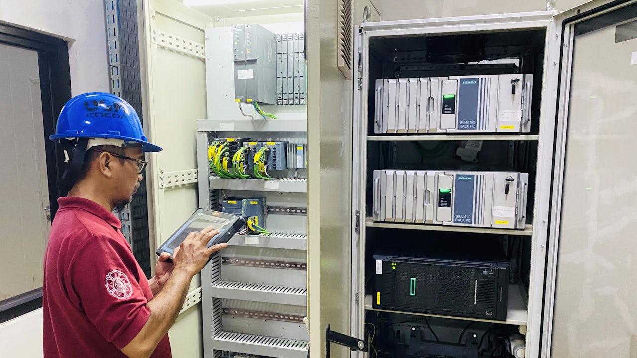 A man wearing a hard hat uses a tablet to check a control cabinet.