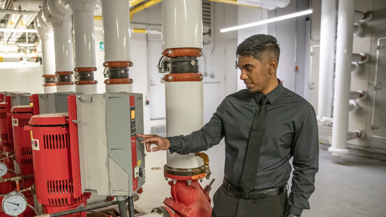 Johnny Ravindran stands in front of a control unit supporting the building’s HVAC system in the UTSC basement. (uuid:fecb070e-c815-4613-b87a-23ed42557a49)