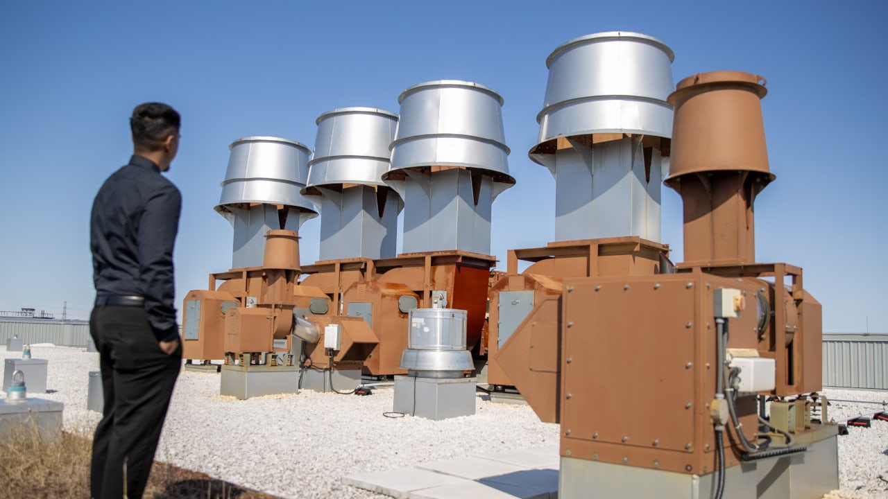 Johnny Ravindran, Manager of Energy Management and Implementation is standing on the roof of the UTSC in front of the roof fans that support the building technology or HVAC system. (uuid:9ab605bc-86c0-4f91-b12f-6b2b714dbfd8)