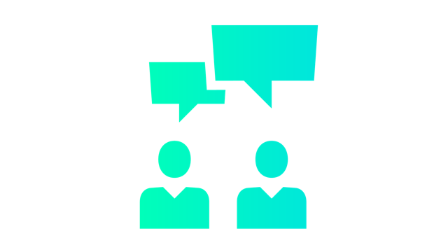 A group of people are sitting around a table, possibly in a meeting, with one person standing and speaking.